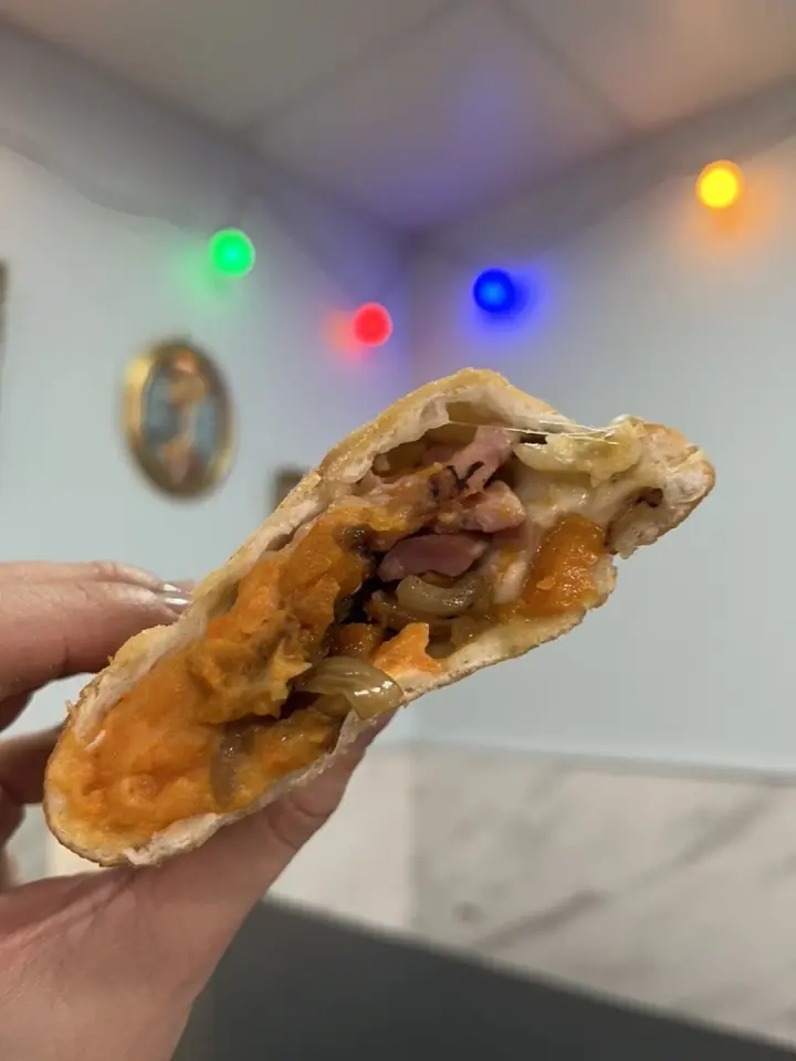 Panzerotto doré ouvert en deux sur sa farce fondante, tenu à la main dans le restaurant. Ori Panzerotti, Montpellier.
