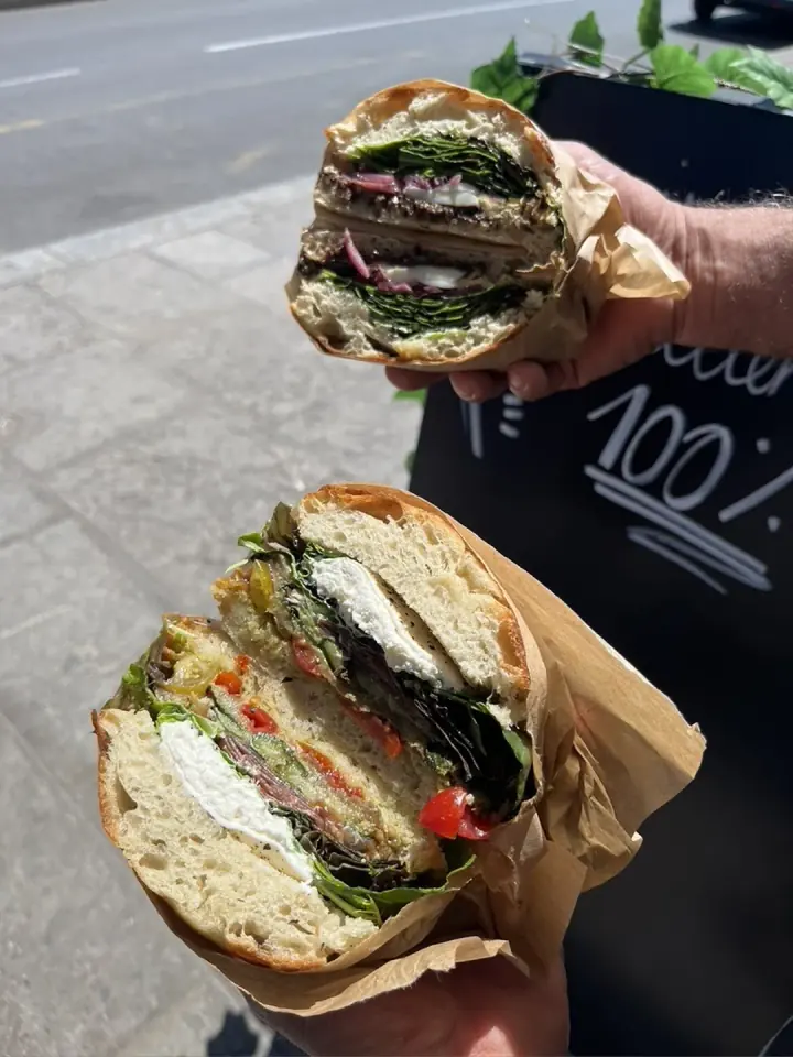 Deux sandwichs focaccia coupés en deux, garnis de légumes grillés, de verdure et de burrata, tenus à la main dans la rue. Ori Panzerotti, Montpellier.